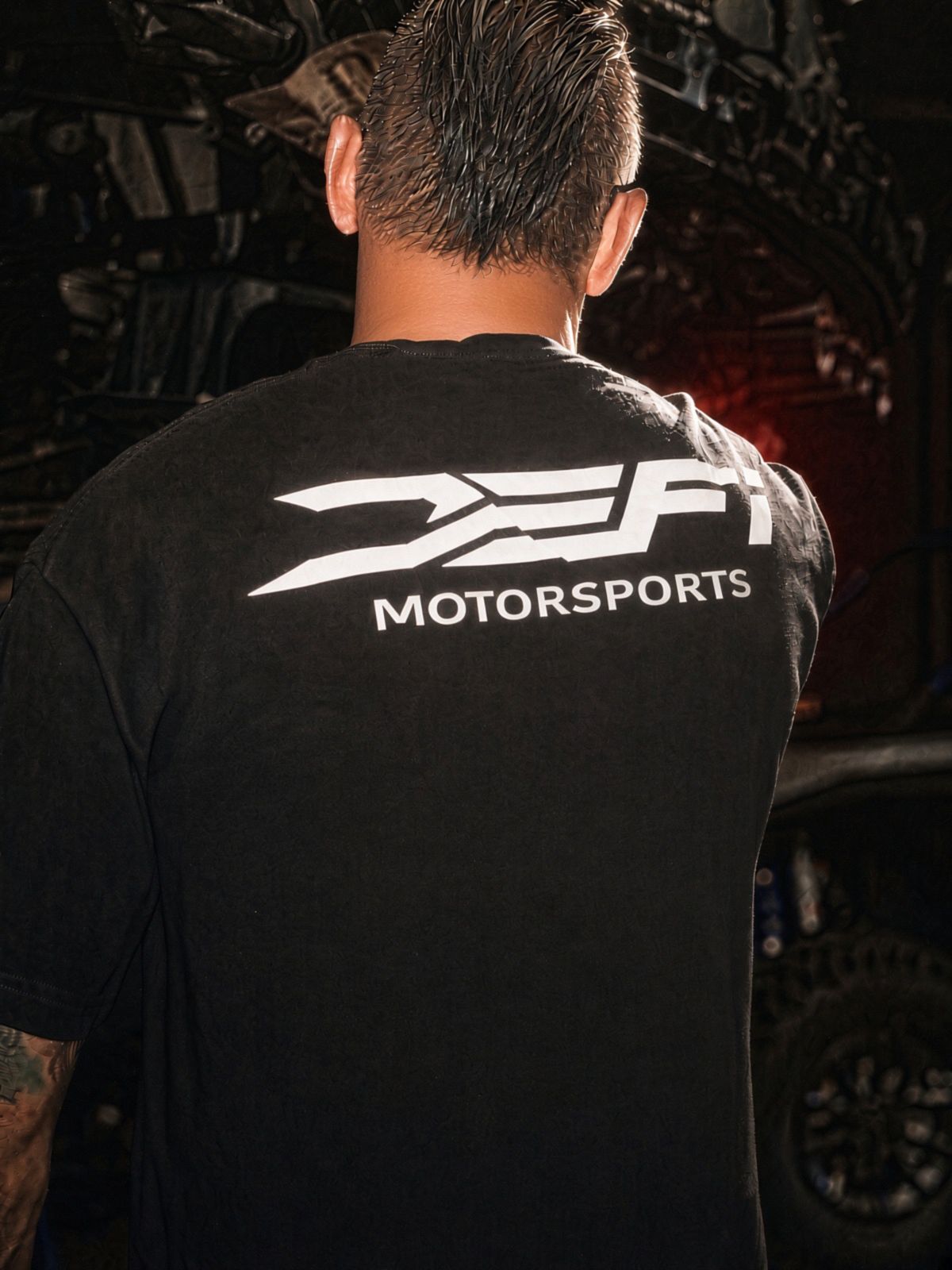 Back view of the black DEFI Motorsports t-shirt with the white lockup, worn in the shop